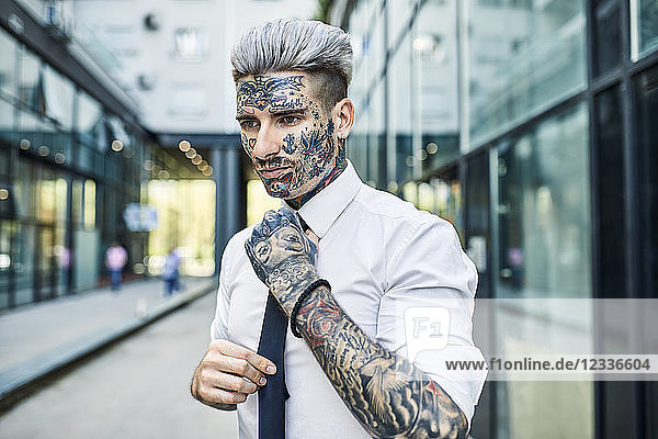 Young businessman with tattooed face  fastening tie