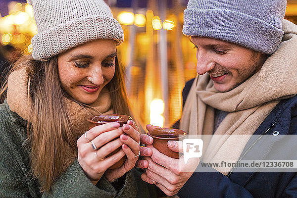 Happy young couple with cups of mulled wine at Christmas market