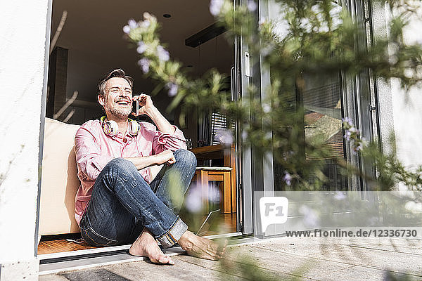 Laughing mature man on the phone sitting at open terrace door