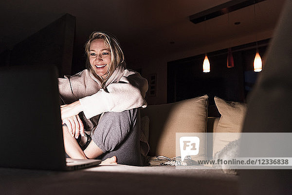 Laughing woman sitting on couch at home looking at laptop