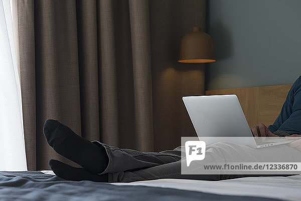 Young man lying on bed using laptop  partial view