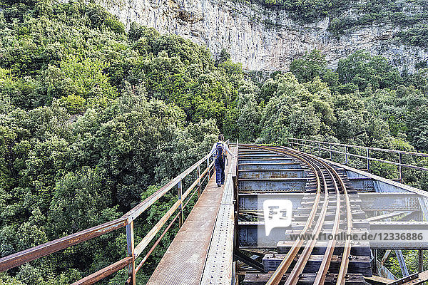 Greece Pilion Milies back view of man walking on bridge along rails of Narrow Gauge Railway