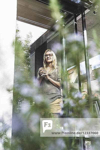 Content mature woman with coffee mug standing in front of her house