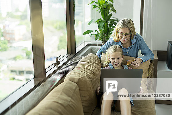 Mother and daughter in modern living room on a couch with laptop and credit card