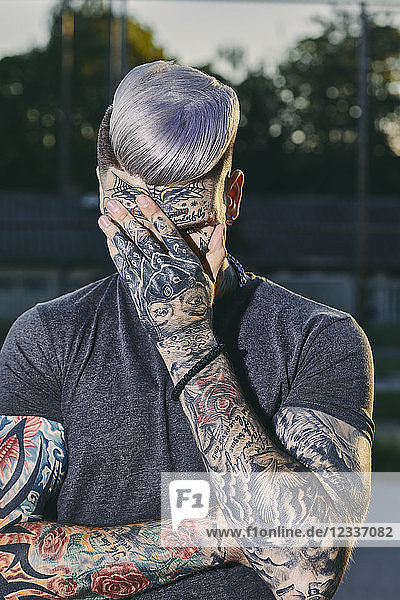Tattooed young man outdoors hiding his face