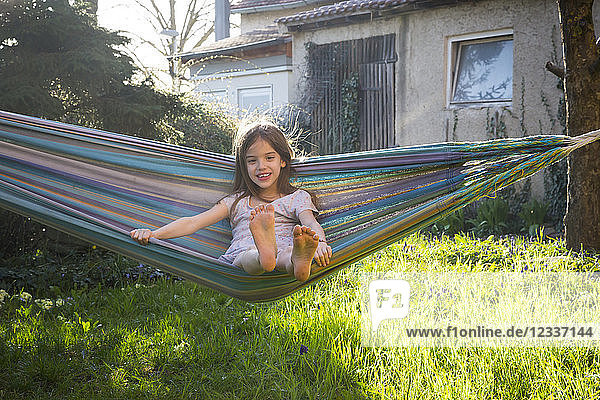 Portrait of smiling little girl sitting on hammock in the garden