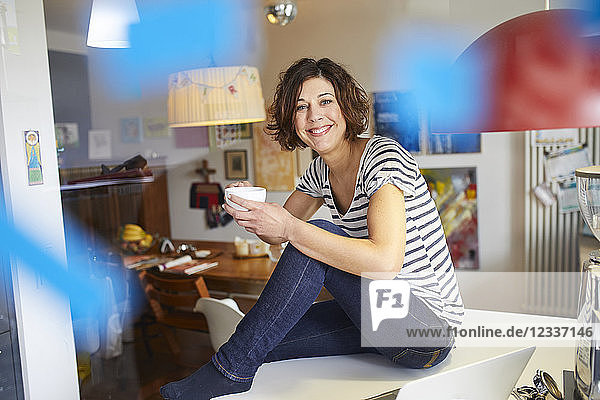 Portrait of happy mature woman sitting with cup of coffee on kitchen table