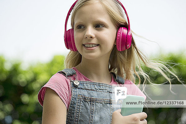 Cute blonde girl listening to music with pink headphones in garden