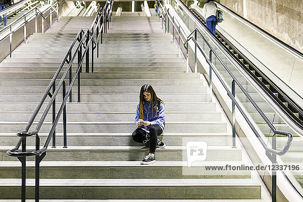 Young woman sitting on stairs using cell phone and earphones