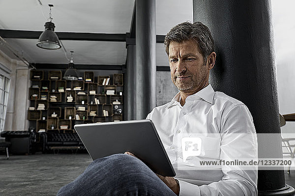 Mature man sitting on the floor using digital tablet in loft flat