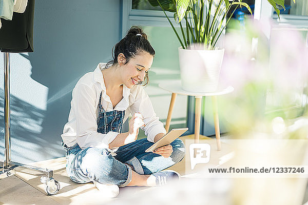 Smiling young freelancer sitting on the floor in her studio using tablet