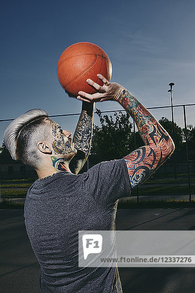 Tattooed young man throwing basketball on outdoor court