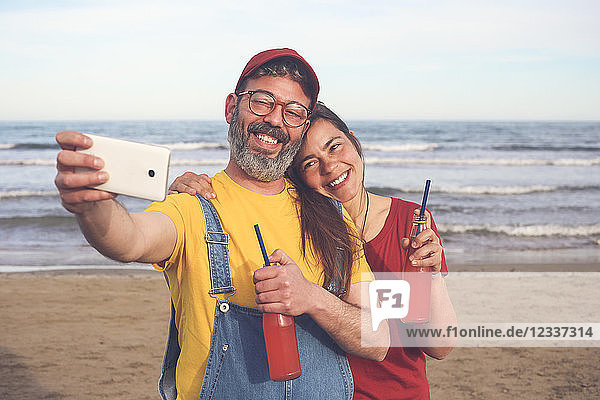 Couple with soft drinks taking selfie with smartphone on the beach