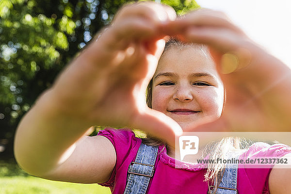Portrait of smiling girl shaping a heart with her hands in park