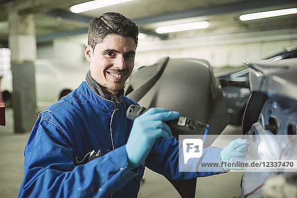 Portrait of smiling mechanic inspecting a car with a torch in a workshop