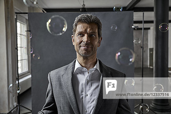 Portrait of mature businessman with bubbles in front of black backdrop in loft