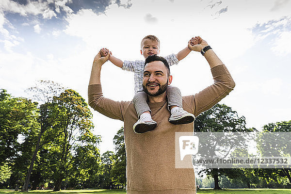 Happy father carrying son on shoulders in a park