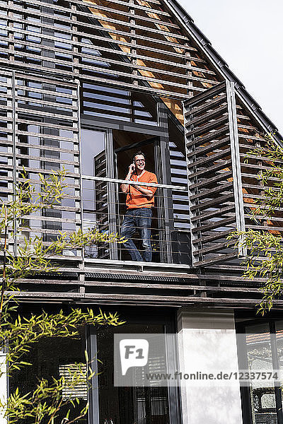 Man on the phone standing on balcony of his house looking at distance
