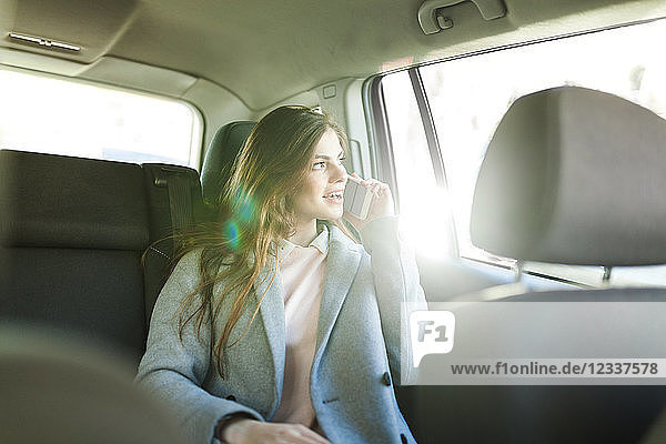 Young businesswoman on the phone sitting on backseat of a car looking out of window