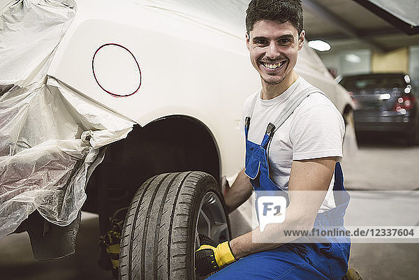 Portrait of smiling mechanic changing car tyre in his workshop