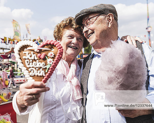 Portrait of happy senior couple with gingerbread heart and cotton candy on fair
