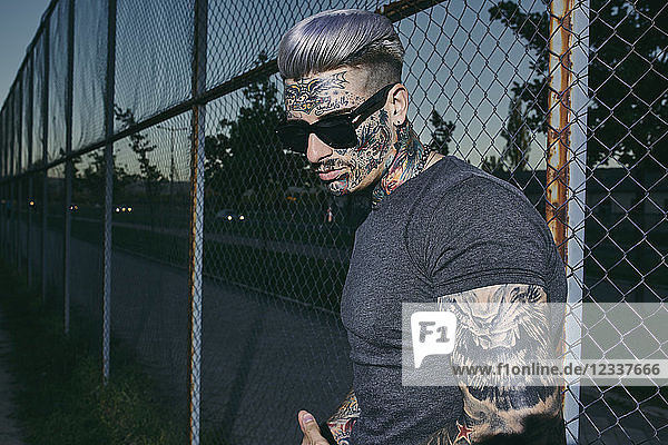Tattooed young man at wire mesh fence wearing sunglasses