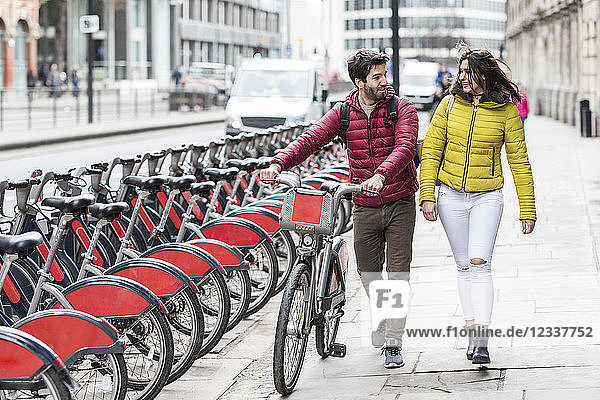 UK  London  young couple with bicycle from bike share stand walking in city