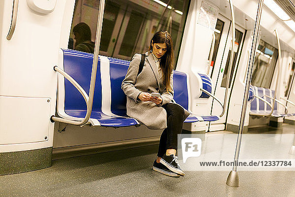 Spain  Barcelona  woman sitting in underground train using cell phone