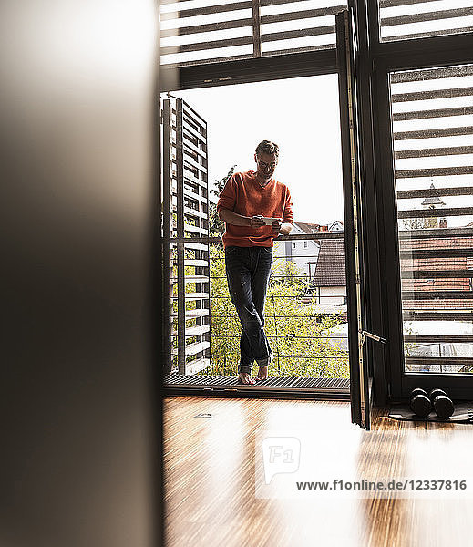 Man standing on balcony of his house looking at smartphone