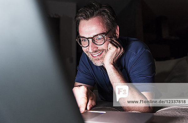 Portrait of smiling man lying on couch at home using laptop
