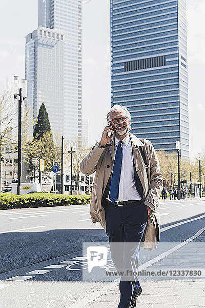 Smiling mature businessman in the city on cell phone on the go