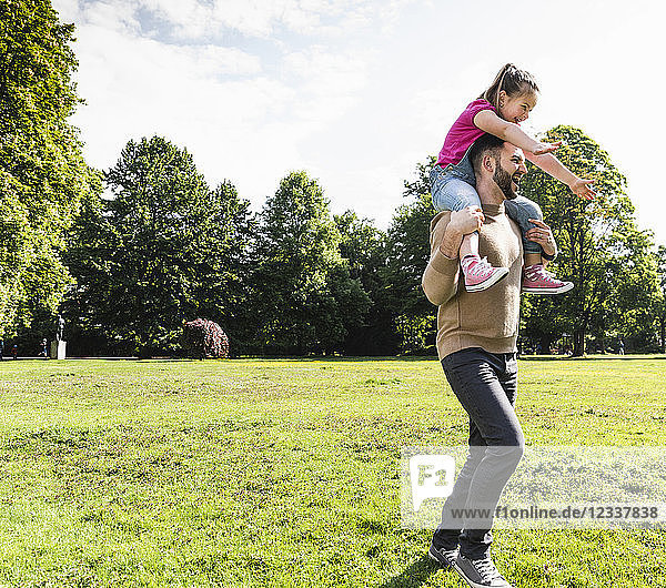 Happy father carrying daughter on shoulders in a park
