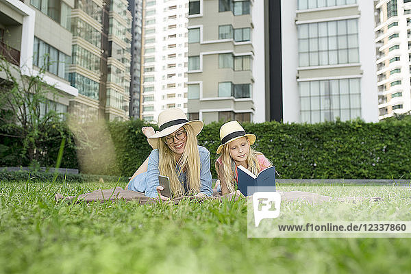 Happy mother and daughter with book and smartphone in urban city garden
