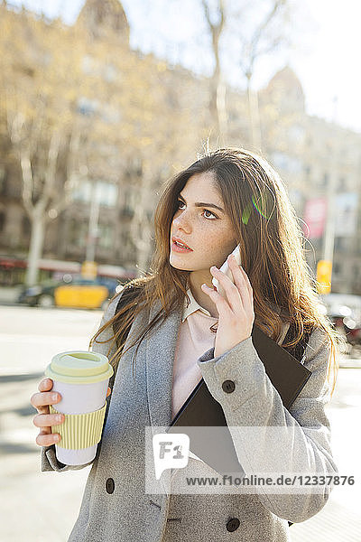 Spain  Barcelona  young businesswoman with coffee to go on the phone