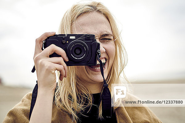Portrait of blond young woman taking photo with camera on the beach