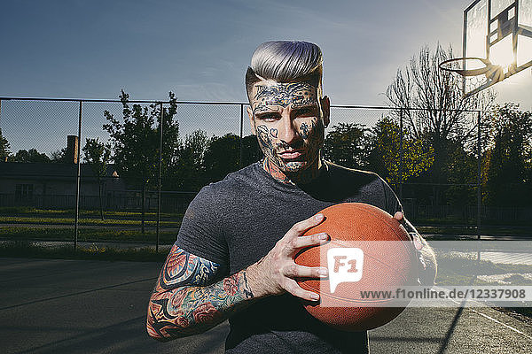 Portrait of tattooed young man with basketball on court