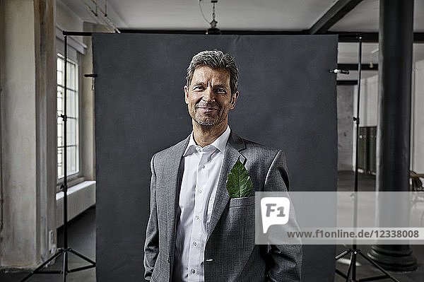 Portrait of mature businessman with leaf in pocket in front of black backdrop in loft