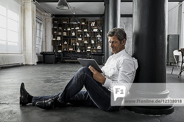 Mature man sitting on the floor using digital tablet in loft flat
