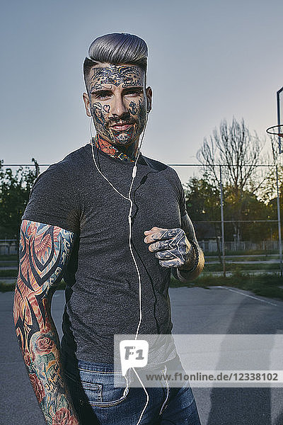 Portrait of tattooed young man listening to music with earbuds