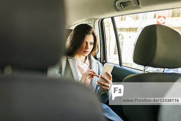 Young businesswoman sitting on backseat of a car using cell phone