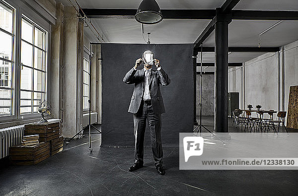 Mature businessman holding refecting mirror in front of black backdrop in loft