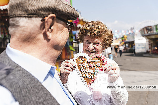 Portrait of hasmiling senior woman presenting gingerbread heart on fair