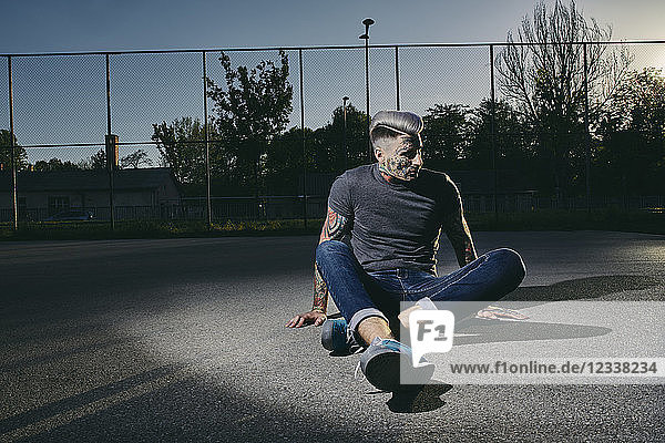 Tattooed young man sitting on basketball court at sunset