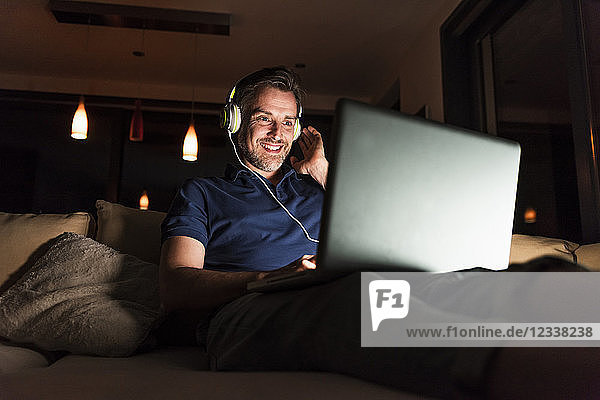 Man with headphones sitting on couch at home looking at laptop