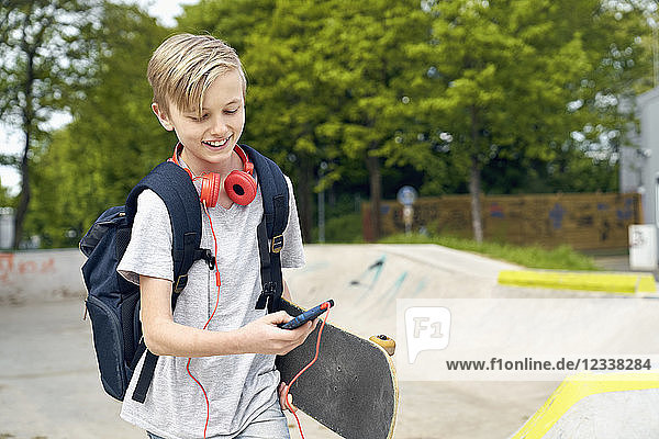 Boy with headphones  skateboard and school bag using smartphone