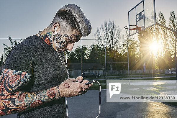 Tattooed young man with smartphone and earbuds