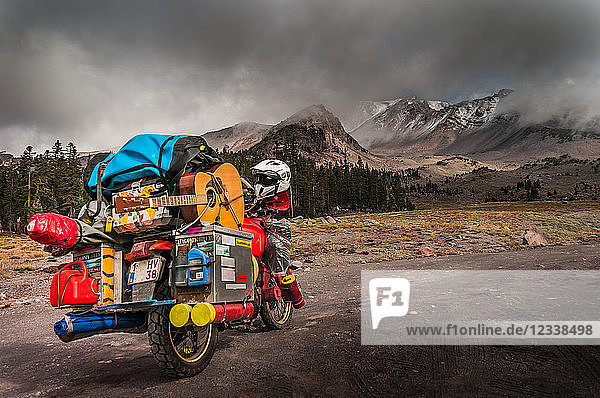 Loaded touring motorcycle on roadside with dramatic sky over Mount Shasta  California  USA
