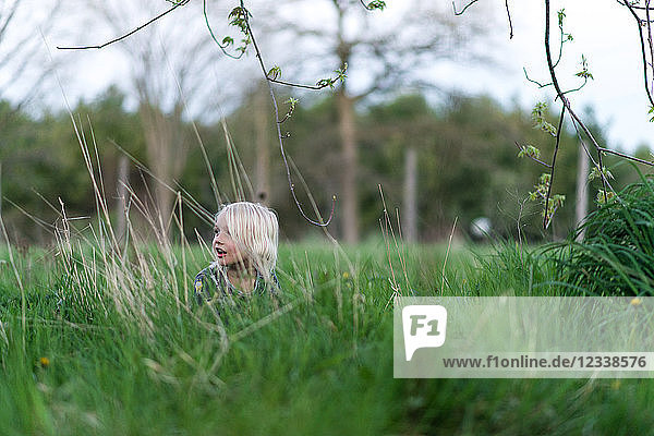 Blondhaariger Junge im langen Gras  der über die Schulter schaut