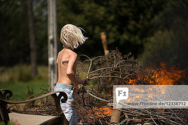 Blondhaariger Junge legt Baumzweig auf Gartenfeuer