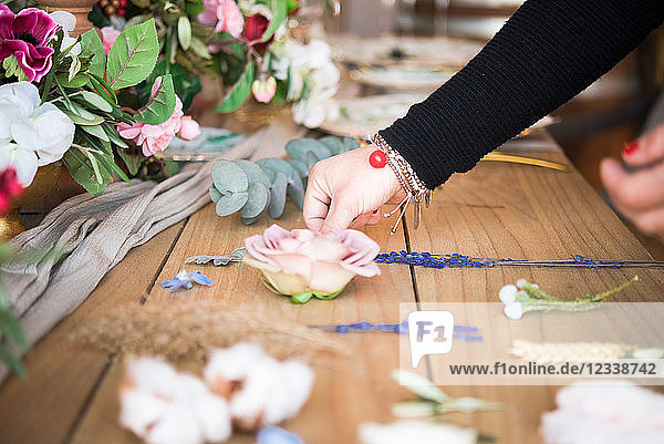 Frau arrangiert Blumenkopf und Stiele auf Holztisch  Detail der Hand